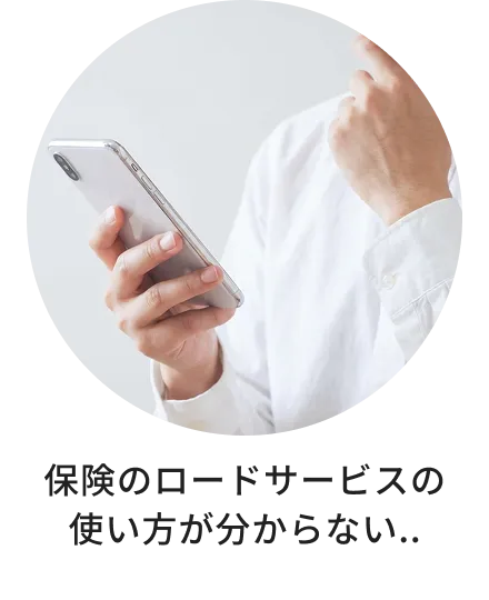 保険のロードサービスの使い方が分からず、スマートフォンを見ながら悩んでいる様子。
            